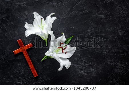 Funeral lily flowers with cross on dark stone background. Mourning symbols