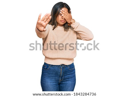 Young latin girl wearing wool winter sweater covering eyes with hands and doing stop gesture with sad and fear expression. embarrassed and negative concept. 