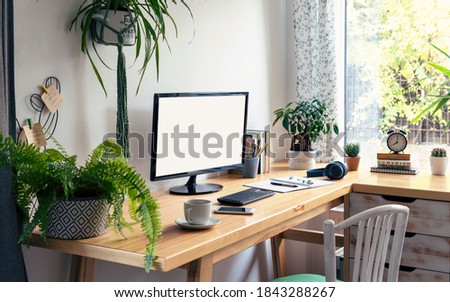 Vintage office desk with monitor with empty screen in vintage office room. Modern workspace with green plants, window and wooden table and decor. Home office.