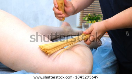 massage therapist makes an anti-cellulite legs massage to a fat woman on a massage table in a spa with a bamboo stick. Spa treatments. Health and beauty, diet. High quality photo