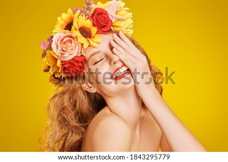 Portrait of a beautiful young woman with long curly red hair and in a wreath of flowers is smiling at camera. Yellow background. Autumn beauty. Make-up and cosmetics.