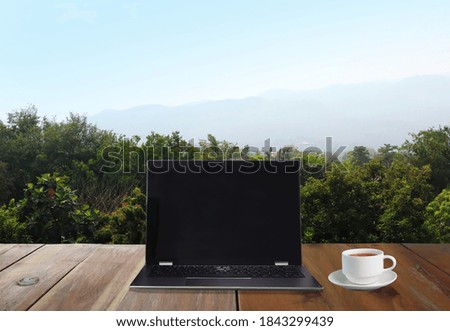 personal laptop computer and a cup of coffee are on the wooden table with background view of forest trees and mountain during work from home sefl quarantine covid19