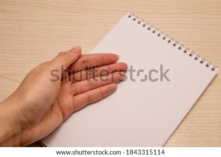 Female left hand lies on a white blank notebook against a wooden background