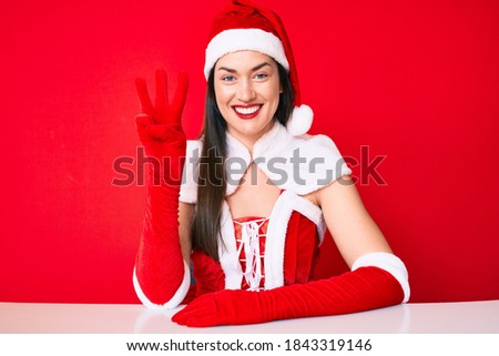 Young caucasian woman wearing santa claus costume showing and pointing up with fingers number three while smiling confident and happy. 