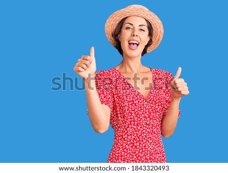 Young beautiful woman wearing summer hat success sign doing positive gesture with hand, thumbs up smiling and happy. cheerful expression and winner gesture. 