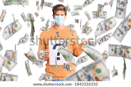 Young handsome man wearing medical mask holding question mark smiling happy pointing with hand and finger to the side