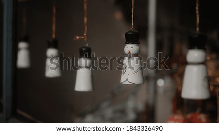 Little white Christmas toys snowmen hang on a thread behind the glass in the house