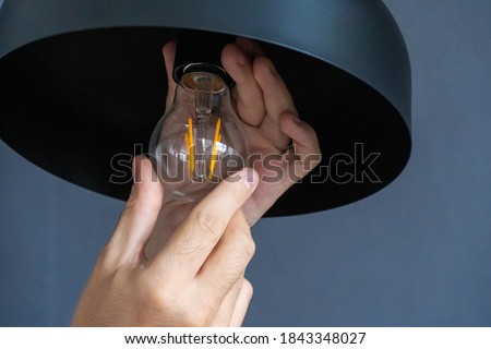 Close-up. A hand changes a light bulb in a stylish loft lamp. Spiral filament lamp. Modern interior decor Royalty-Free Stock Photo #1843348027