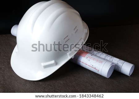 White hardhat and rolled engineering drawings at engineer workplace.
