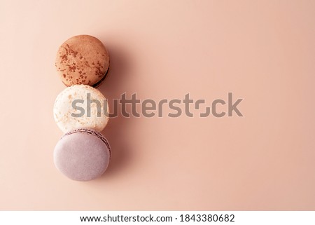 Three macaroons chocolate, vanilla and berry on pastel background for your design. Food concept in vintage style. Copy space. Closeup. Flat lay style.