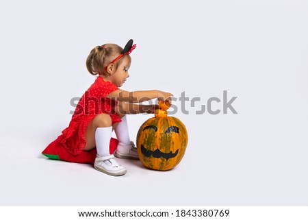  A little girl in a red dress is enthusiastically playing with pumpkins. Autumn day. Halloween.