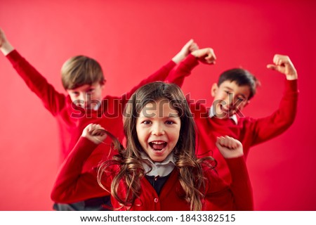 Portrait Of Excited Elementary School Pupils Wearing Uniform Having Fun On Red Studio Background Royalty-Free Stock Photo #1843382515