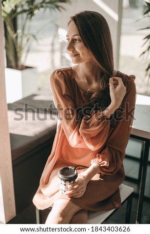 Young happy woman sitting at a table and drink cup of coffee in a paper cup in a cafe. The girl starts the morning with a cup of drink. businesswoman, meeting, style, romantic, happy