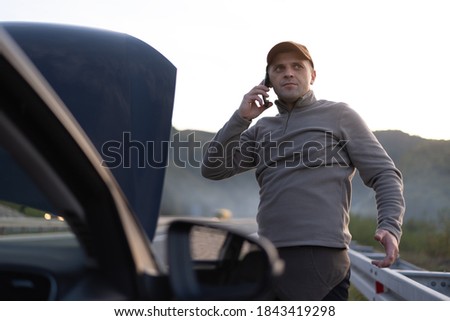 Frustrated and angry man calls roadside assistance by phone. car problem. Roadside assistance concept