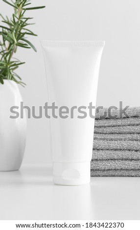 White tube cream mockup with towels and a rosemary on a white table.