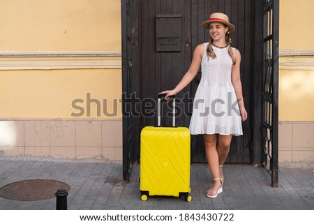 A traveler girl with a yellow suitcase in her hand stands at the door of the hotel.