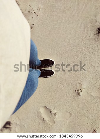 Photo of standing legs in jeans and sneakers on white sand. View from above