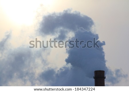 Smoking stack of an old thermal station against a sun in the overcast day Royalty-Free Stock Photo #184347224