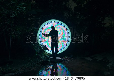 One person standing alone against a green and white circle light painting as the backdrop