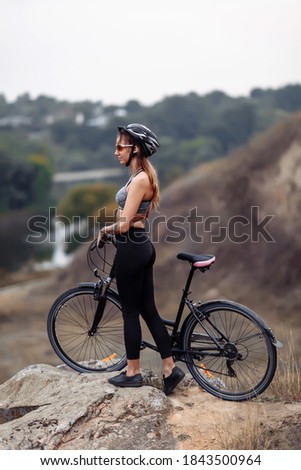 Fit young woman wearing sportswear standing with her bicycle on rocky background at autumn day