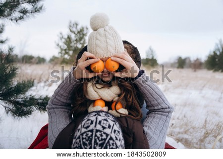 Young couple fooling around in the snow in winter. the man covers the woman's eyes with tangerines. High quality photo