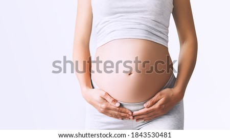 Pregnant woman holds hands on her belly on white background, close-up. Beautiful photo of pregnancy. Mother waiting for baby. Women prepare for maternity. Concept of prenatal period, maternal health. Royalty-Free Stock Photo #1843530481