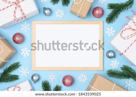Wooden frame with white place for text. New Year's fir branches with Christmas tree decorations and snowflakes. Xmas gifts on a light blue background. Flatlay. Copy space. Nobody.