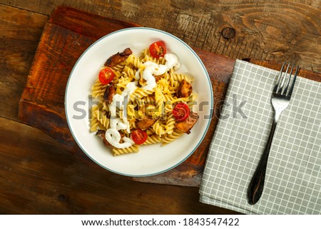 Pasta with chicken and cheese in a gray plate on a stand on a napkin with a fork.