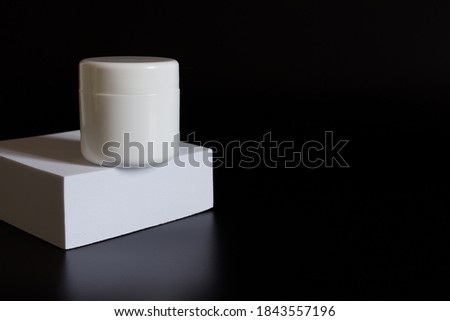 white rectangular box with shadows on a black background. White plastic cream jar. For cosmetics or cosmetology background. stand for advertising beauty products. Plants decor eucalyptus, fern, spruce