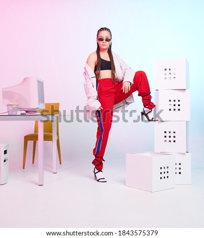 Cool young female office worker in sunglasses with old computer monitor and boxes. Colored Neon light