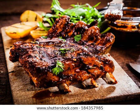 Delicious barbecued ribs seasoned with a spicy basting sauce and served with chopped fresh herbs on an old rustic wooden chopping board in a country kitchen Royalty-Free Stock Photo #184357985