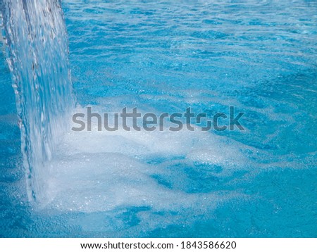 Background of bubbles created by a small waterfall in the blue water of a swimming pool on a bright sunny day with copy space.