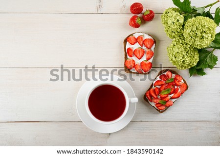 morning Breakfast concept, tea with hibiscus, sandwich with strawberries and cottage cheese, flowers on white wooden background, still life, copy space, top view