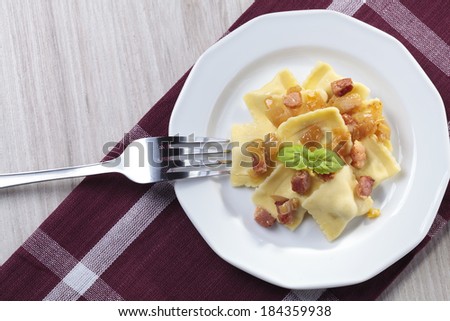 Portion of ravioli with onion and bacon on white plate