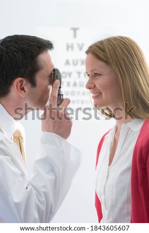 An ophthalmologist examining a smiling blond woman's eyes with an ophthalmoscope