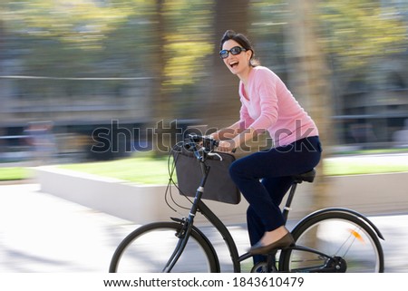 Horizontal panning shot of a joyous businesswoman riding a bicycle outdoors looking at the camera with copy space.
