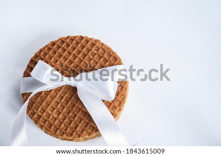 Stack of round waffles with caramel in the lower left corner, with white gift ribbon, bow on a white background, with space for text. Selective focus
