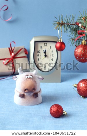 Symbol of 2021 - bull - on the background of a clock and a new year's gift with red Christmas balls, blue background, vertical frame
