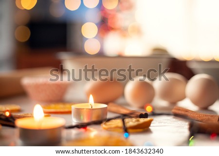 Candles and colorful lights, eggs, dried orange and cinnamon sticks close-up on the table in the kitchen. Christmas decoration, baking, cozy atmosphere.