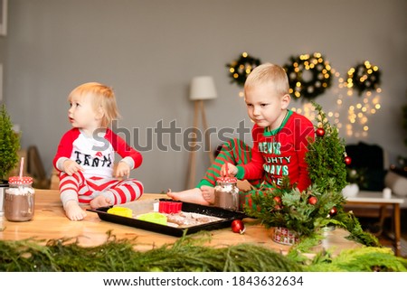 Boy and one-year-old girl drink Christmas cocoa amd make cookies in the kitchen.