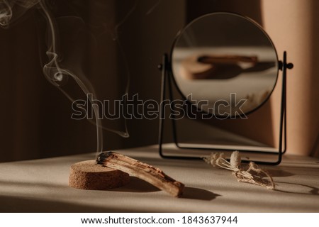  palo santo with jet of smoke, mirror and dried flowers on a neutral background. Abstract trendy picture. Minimalistic wabi sabi style.