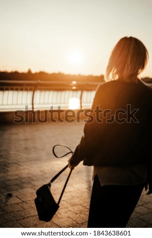 Beautiful young woman walks towards dawn with a handbag in the city. Orange warm highlights in the photo. Blurry motion. Concept. Background. Inspiration, motivation to move forward