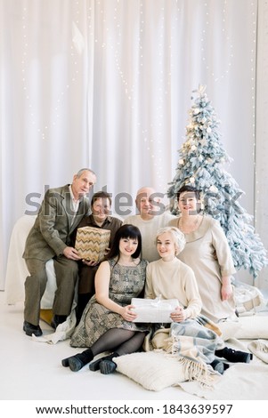 Multi Generation European Family, celebrating winter holidays together, exchanging and opening Christmas presents, sitting in front of beautiful decorated Christmas Tree