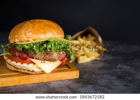 
Delicious fresh burger with cheese and cutlet and fries in the package. Food for the menu of cafes and restaurants. Fast food is harmful to the body and diet. Street food. Free space for the menu.