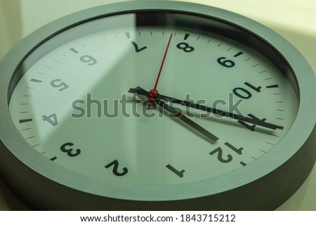 It's five to twelve, the clock is ticking. Modern white clock shows the time 5 before 12. Close up to a wall clock, with five minutes to twelve o'clock. Running out of time for crisis management
