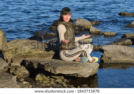 Young attractive woman sitting on the beach on the rocks and doing breathing exercises, meditation and relaxation concept, healthy lifestyles, travel and tourism outdoors