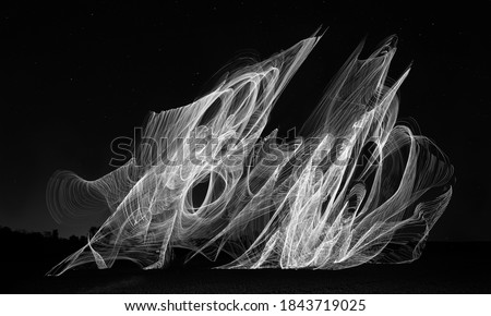 black and white composite of stunt kite in flight with lights mounted to it at night, light trails