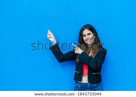 Latin woman in red and black clothes looking to the camera pointing with two hands and fingers to the side