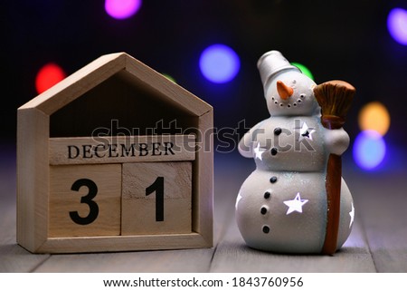 Christmas decorations on a wooden background: cubes with the numbers December 31, glowing snowman and blurry garland in the background