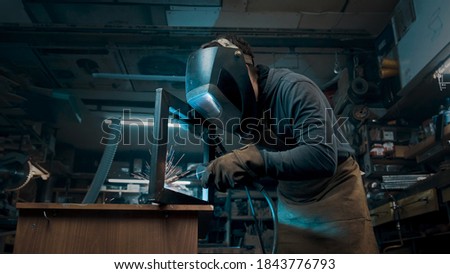 Worker wearing a mask and gloves soldering metal parts Royalty-Free Stock Photo #1843776793